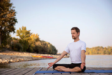 Fototapeta na wymiar A caucasian men parcticing yoga on pier by lake