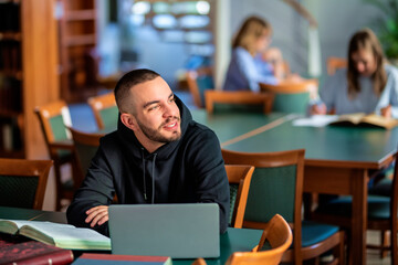 Confident male university student sitting in the library and studying