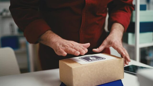 Closeup of man putting fragile handle with care sticker on a box for delivery