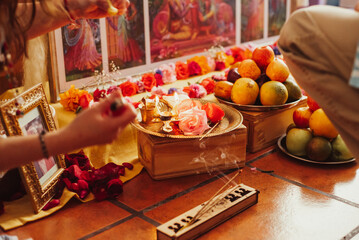 Preparing a colourful Hindu altar with offerings for a kirtan celebration honoring Krishna an other deities of the religion with mantras, incense, roses, fruit and a puja cleansing with the elements