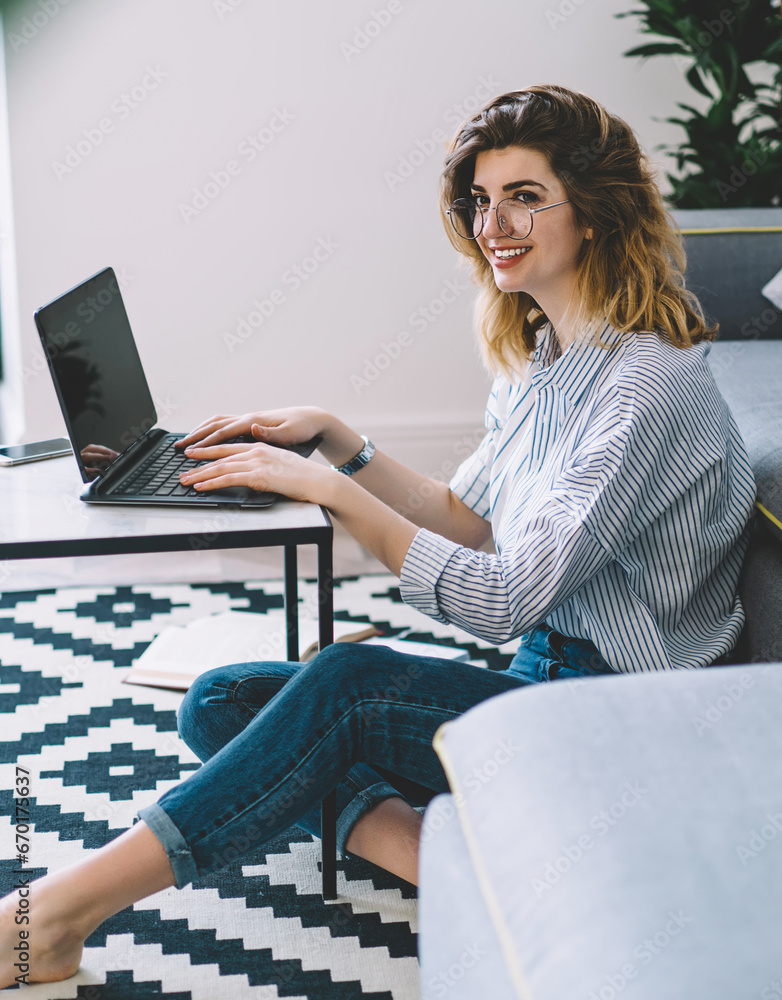 Poster smiling hipster girl sitting on floor in flat and studying at netbook
