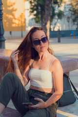 Young woman poses in a small town with her cell phone and sunglasses