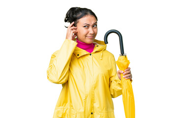 Young Uruguayan woman with rainproof coat and umbrella over isolated chroma key background having...