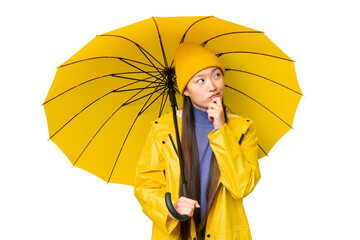 Young Asian woman with rainproof coat and umbrella over isolated chroma key background and looking...