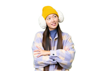 Young Asian woman wearing winter muffs over isolated chroma key background looking up while smiling
