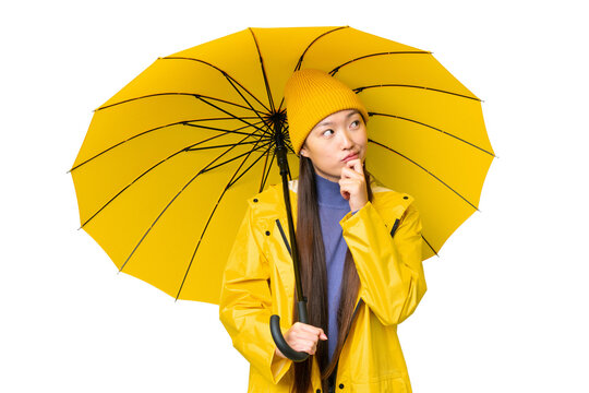 Young Asian woman with rainproof coat and umbrella over isolated chroma key background and looking up