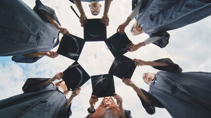 Graduates in black robes join their caps in a circle.