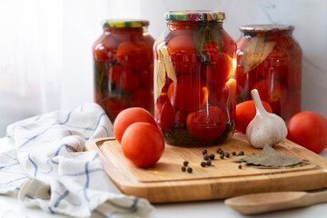 red tomatoes in canned jars stand on the kitchen table next to garlic and peppercorns