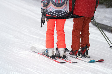 Paired uphill climb on t-bar. Fragment of skiers: skis, legs and ski poles in hands.