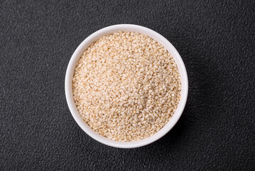 Raw white sesame seeds or grains in a bowl on a textured concrete background