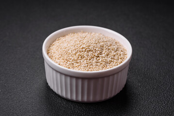 Raw white sesame seeds or grains in a bowl on a textured concrete background