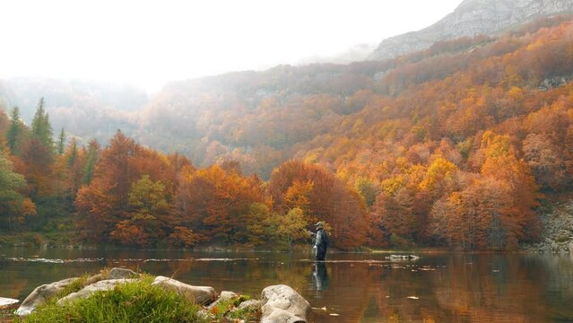 Pescando a mosca in un lago sulle alpi italiane circondato da alberi immersi nel colori dell'autunno