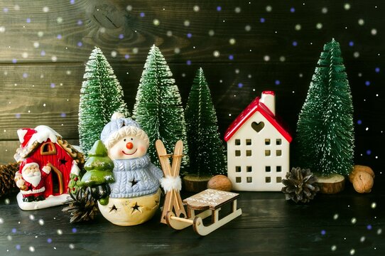 Christmas card, porcelain toy snowman with a Christmas tree in his hands and a New Year's forest house, green Christmas trees and a wooden sleigh.  Home decoration.  Background picture.