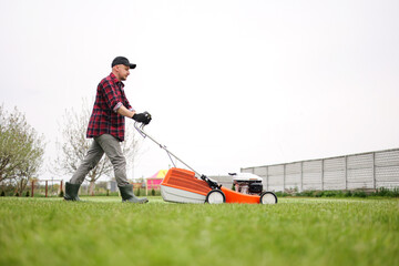 view of man in casual clothes mows lawn with lawn mower at backyard of his house. Husband takes...