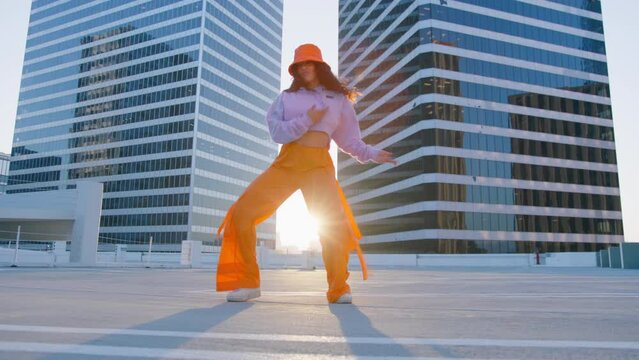 Young mixed race carefree girl enjoys sunset and dancing. Black lady performing RnB moves in city cinematic RED camera. Happy beautiful african american woman dancing outdoor in downtown at sunset 4K