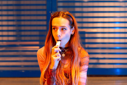 Young woman vaping near blue metallic backdrop