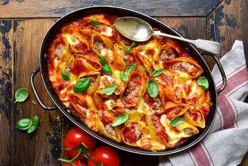 Stuffed pasta cannelloni with minced meat baked in  tomato sauce in a skillet. Top view with copy space.