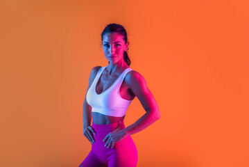 Sportive beautiful woman training with athletic body and sportswear doing workout, colorful lighting and background