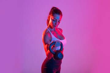 Sportive beautiful woman training with athletic body and sportswear doing workout, colorful lighting and background