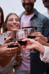 Vertical photo focus on red wine glasses. Friends toasting, celebrating together. People having fun outdoors. Copy space.