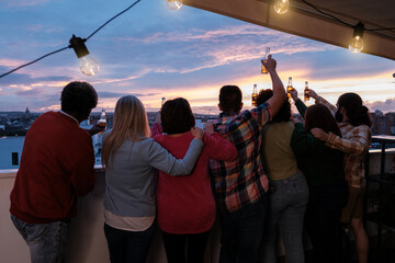 Unrecognizable and diverse group of friends gathered on a terrace watching the sunset and toasting....