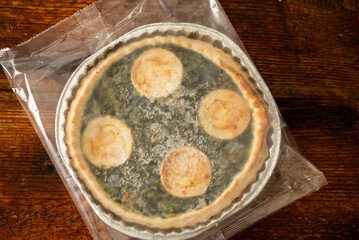 An image of a frosty cheese and spinach pie placed against a rustic wooden backdrop