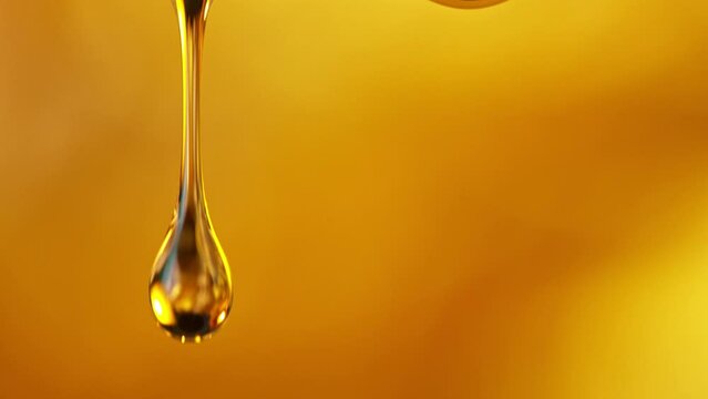 Super Slow Motion Shot of Falling Golden Oil Droplets Isolated on Orange Background at 1000 fps.