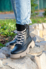 Female legs in black boots on a background of stones. The atmosphere of an autumn day. Lifestyle.