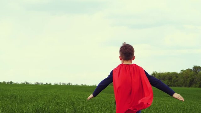 The superhero is running through a green meadow against a horizon of blue sky. The boy runs with his arms out to the sides, mimicking flight. A red cape slowly develops on the super hero back. power