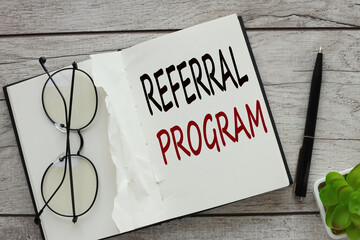 a notebook with glasses on it. words Referral Program