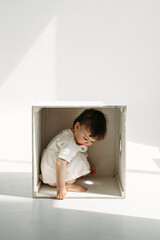 A little one-year-old girl is playing, climbed into a wooden cube - a chair.
