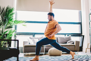 Side view of sportive young man holding hand up during morning workout at home apartment