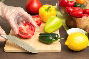 Cooking vegetables. Chef hand cutting tomato and different vegetables for salad close up. Hands in gloves cooking healthy vegetarian vegan diet food