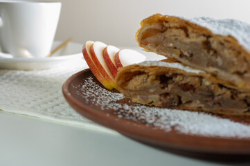 Paired pieces of delicious strudel stuffed with apples and cinnamon on a light plate on a light background. Place for writing. Close up view. Homemade Ukrainian pastries