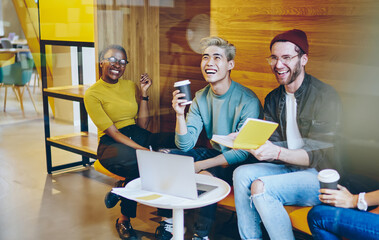 Cheerful multicultural young people laughing during coffee break in modern office - obrazy, fototapety, plakaty