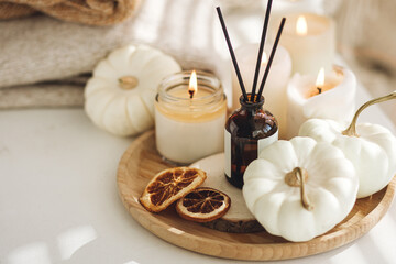 Obraz na płótnie Canvas Autumn cozy mood composition on the windowsill. Aroma diffuser, pumpkins, dry citrus, candles on wooden tray, knitted warm plaid. Fall hygge home decor, aromatherapy. Copy space, white background