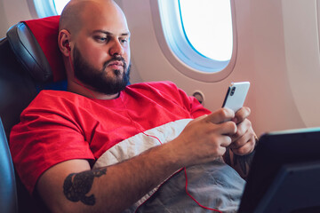  Young man tourist listening music and browsing network on cellular during flight