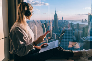 Hipster girl traveler enjoying panoramic view of New York downtown and studying with audio book - obrazy, fototapety, plakaty