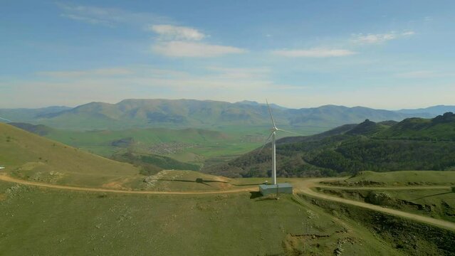 Wind turbines on the mountain against the blue sky. On the hills are trees and country roads. Renewable energy concept. Drone video. Flying sideways. Pushkin Pass.
