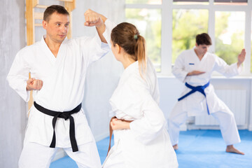 Fototapeta na wymiar Young guy and woman during martial arts class train to perform basic blows to opponent with hands and feet. Preparation of athletes for competitions. Third male partner performs warm-up before lesson