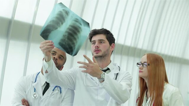 Three confident doctor examining x-ray snapshot of lungs in hospital