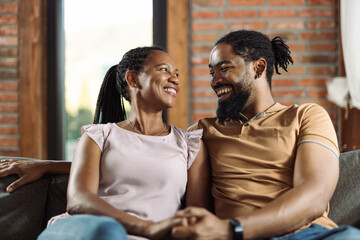 Happy black couple talking while relaxing on sofa at home