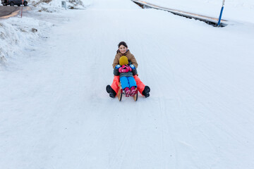 Fototapeta na wymiar wide angle view of two girls sledding on snow slope at wooden sleigh one child closes eyes with hands