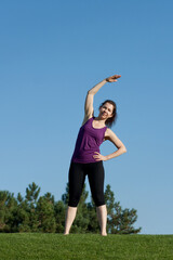 Athletic young woman doing warm-up before fitness workout in park, blue sky background
