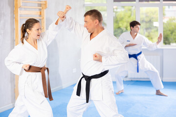 Woman and man in kimono sparring together in gym during karate training