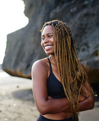 Cheerful dark skinned sportwoman dressed in active clothes smiling near rocks