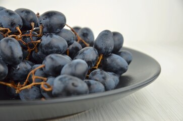Clusters (bunch, branch) of black grapes on a black plate on a white background, side view, closeup