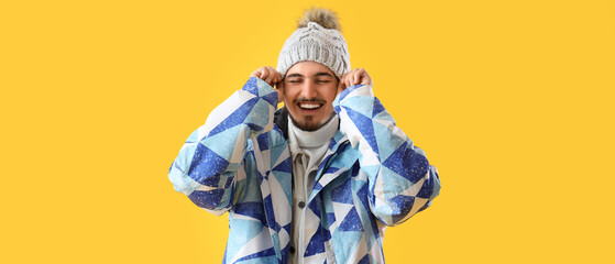 Stylish young man in winter clothes on yellow background