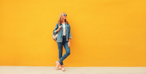 Fototapeta premium Full length beautiful smiling young woman wearing denim jacket, backpack on yellow background