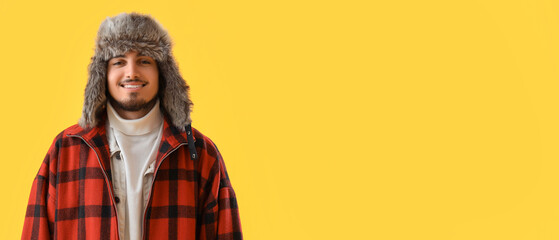 Stylish young man in winter clothes on yellow background with space for text